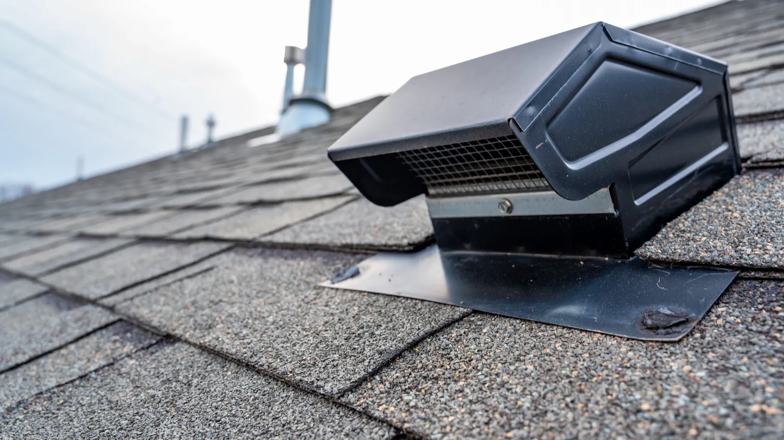 Metal flashing and a black roof vent cap mounted on shingles